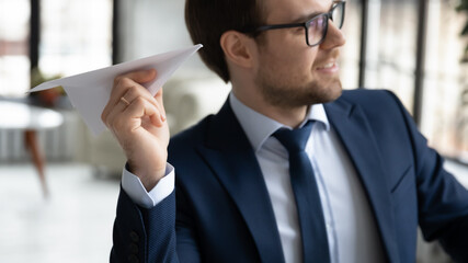 Close up of excited young male CEO or director hold throw paper plane have fun rest in office. Millennial businessman feel motivated entertain at workplace. Startup launch, business project concept.