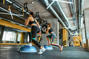 Full length of two young athletic women in sportswear exercising together with resistance fitness...