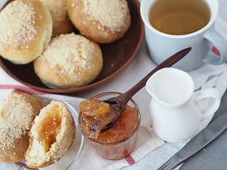 Round buns with filling in a natural wicker plate for tea and apple jam on a gray background. Ready to eat. Home cooking concept.