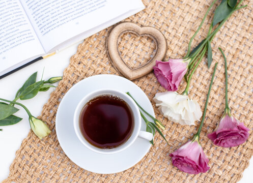 Morning time, beautiful picture for blog post in Instagram. Relax and have cup of coffee or tea on brown napkin decorated by flowers, heart and book. Enjoy your free minutes. Layout.