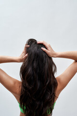 Rear view of young woman wearing green underwear posing against light background, showing off her healthy long dark brown hair