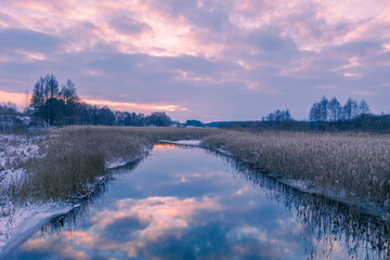 Rural landscape in winter. View of a brook and cloudy sky at sunset