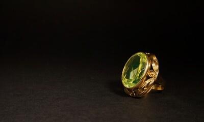 Women's gold ring, green gemstoneon a black background
