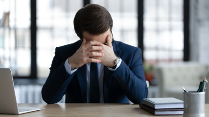 Upset distressed young Caucasian businessman sit at table in office think of business problem...