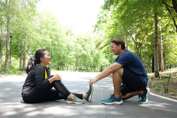 Asian young woman in sportwear is Cramping her leg and boyfriend helping for relaxation of resilient and Muscle contraction after excersice and running in the Garden. Healthy on holiday Concept
