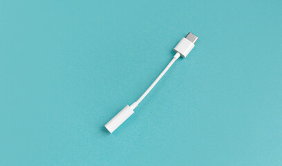 An adapter for a USB to 3.5mm type c headphone cable on a smartphone. white cable and 3.5 audio cable for phone on android mm on a blue background. View from above. copy space.