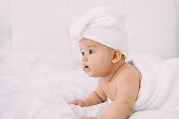 The girl lies on a white bed with a towel on her head and body. Hygiene and baby care concept.