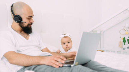 Obraz premium A young dad is sitting on a bed with a child together at home at a computer. A father works on a laptop.