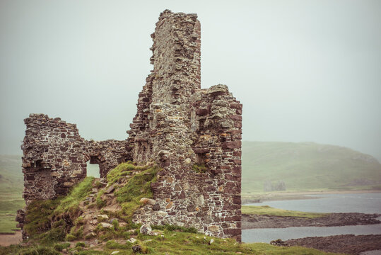 Castle ruins on moody loch water surrounded by misty mountains
