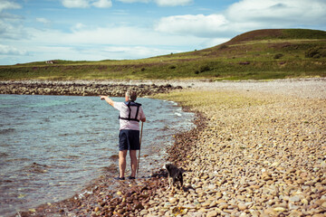 Retired man and dog point on rocky beach island in remote scotland