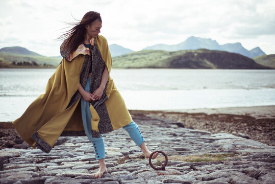 girl in cloak leans on stone jetty circle dock in mountains