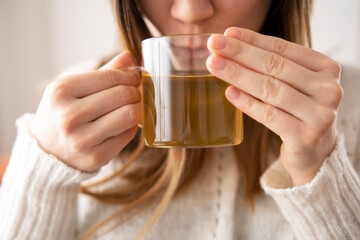 Blonde woman in white sweater drinking her green tea.Spend time at home in winter.Healty herbal tea and antioxidant source.