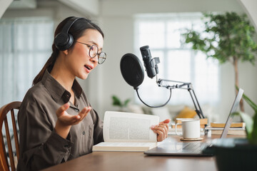 Asian woman recording a podcast on laptop computer with microphone while online live streaming at...