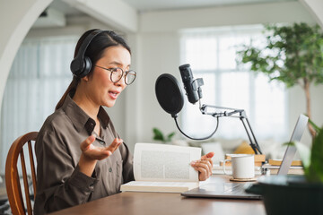 Asian woman recording a podcast on laptop computer with microphone while online live streaming at...