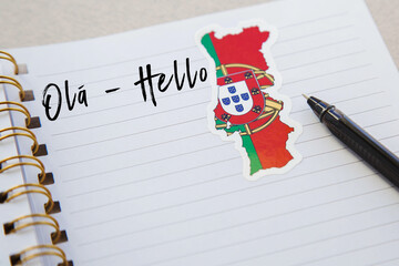 notepad with the words hello in portuguese language, portuguese flag and country map, pen, foreign...