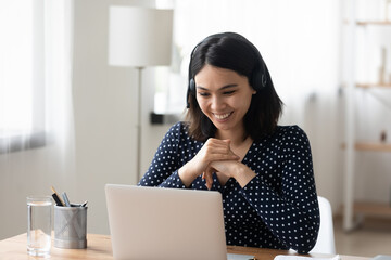 Young mixed race female in bluetooth headset have nice talk conversation via pc webcam. Friendly asian woman english language tutor give remote lesson before computer screen teaching pupil on distance