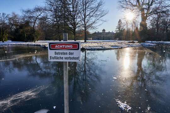 Warning sign with the inscription "Caution, keep off the ice surface" at the frozen pond of Schloss Favorite palace garden in F&ouml;rch, Germany