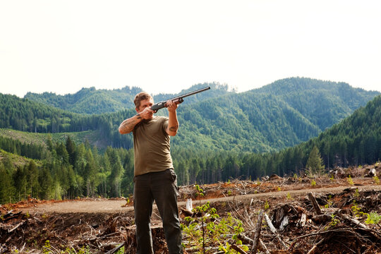 Hunter aiming with rifle while standing against clear sky