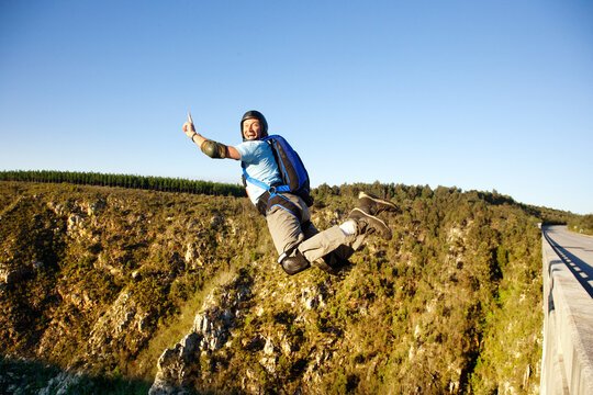 Side view of man base jumping against clear sky
