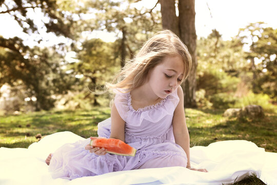 Girl with watermelon sitting on blanket in backyard