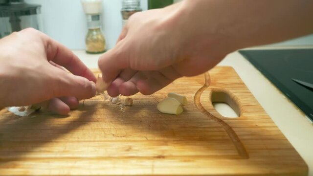 close-up of male hands chopping garlic on a wooden cutting board.