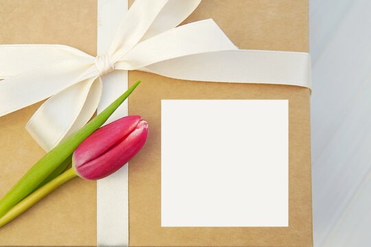 Square card or sticker mockup on gift box decorated with white ribbon and tulip, Mother's day, Woman day greetings.