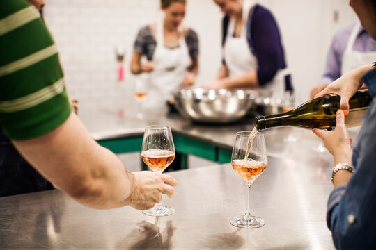 Cropped image of woman pouring wine while standing by coworkers at commercial kitchen