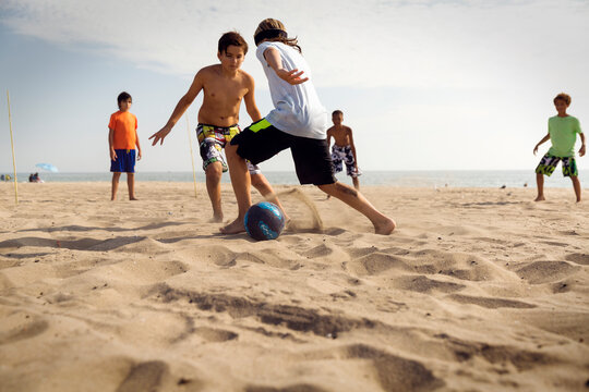Friends playing soccer at beach against sea