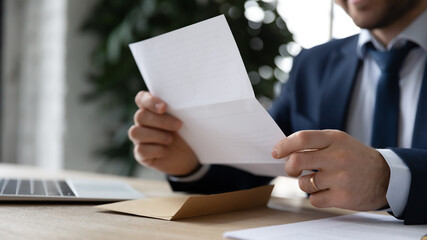Crop close up businessman sit at desk reading post paper letter or correspondence in office. Male...