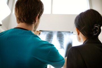 Rear view of doctor showing x-ray to businesswoman in hospital