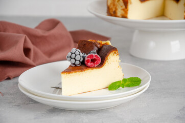 San Sebastian cheesecake with berries and mint leaves on top on a white plate on a gray concrete background. Traditional Spanish dessert. Copy space