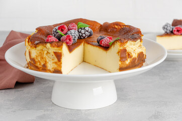 San Sebastian cheesecake with berries and mint leaves on top on a white plate on a gray concrete background. Traditional Spanish dessert. Copy space