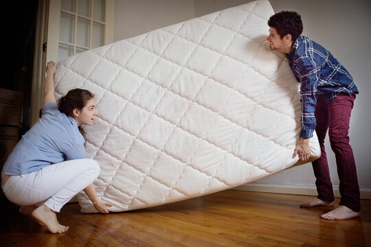 Couple carrying mattress in room