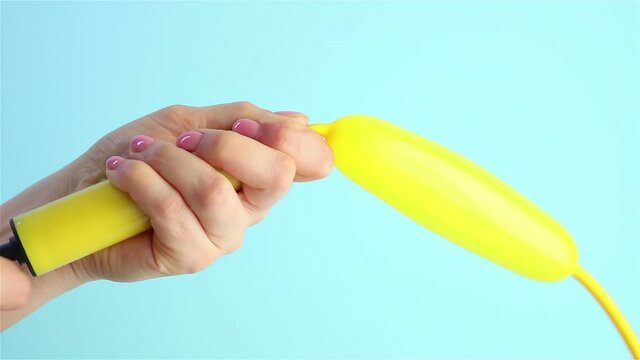 woman hand  inflates a yellow balloon with air pump blue background close up