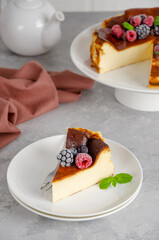 San Sebastian cheesecake with berries and mint leaves on top on a white plate on a gray concrete background. Traditional Spanish dessert. Copy space