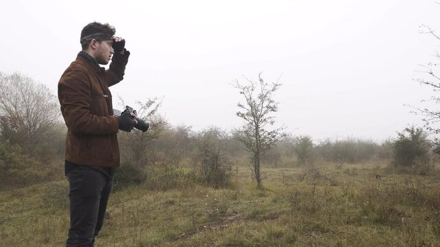 Wildlife photographer observing his surroundings in a misty steppe.