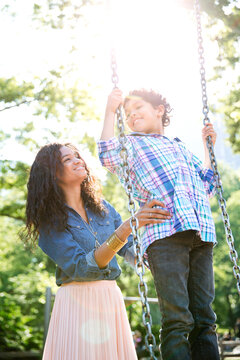 Mother pushing son standing on swing