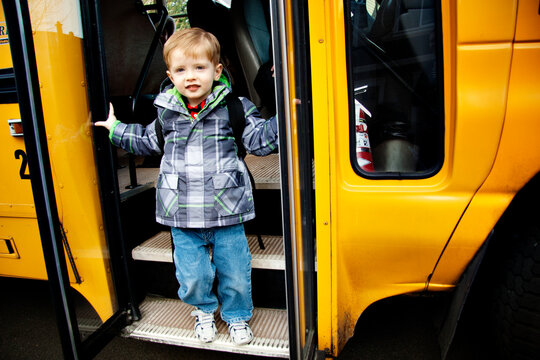 Portrait of cute boy with backpack standing on steps of school bus