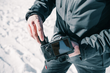 Hands of a photographer inserting the battery into his professional camera in the snow.