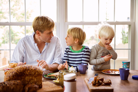 Father and sons talking while having food at table against window