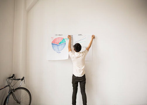 Rear view of businessman sticking charts on white wall at creative office