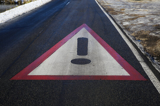 Close up of red white triangle danger warning sign on asphalt of slippery icy  road with snow and black ice 