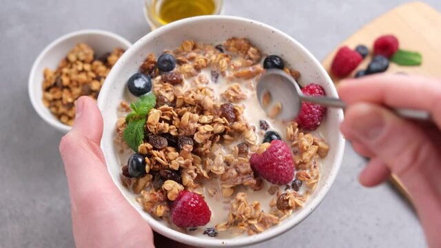 Eating granola with raisins and berries. Healthy breakfast bowl in hands. Clean eating, dieting concept