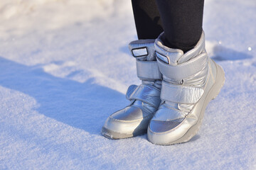 Children's winter boots in silver color on the snow