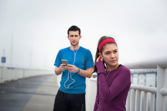 Confident female athlete wearing earphones while standing with friend on Bay Bridge