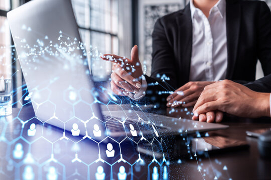 Two HR specialists analyzing the recruitment market using laptop to boost the intern program at international consulting company. Social networking hologram icons.