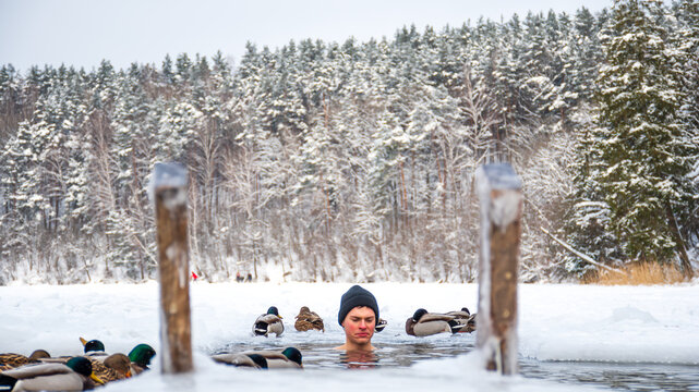 Beautiful boy bathing and swimming in the cold water of a lake or river among the ducks, cold therapy, ice swim with forest trees on background