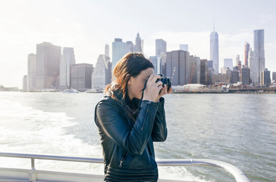 Side view of woman photographing while standing on boat against cityscape