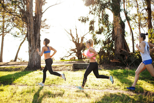 Female athletes jogging by trees on field against clear sky - Powered by Adobe