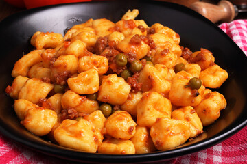 Gnocchi di patate al ragù di carne con piselli in un piatto di ceramica scura.